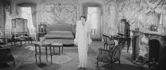 Wide shot frame from L'année dernière à Marienbad — standing, room, table