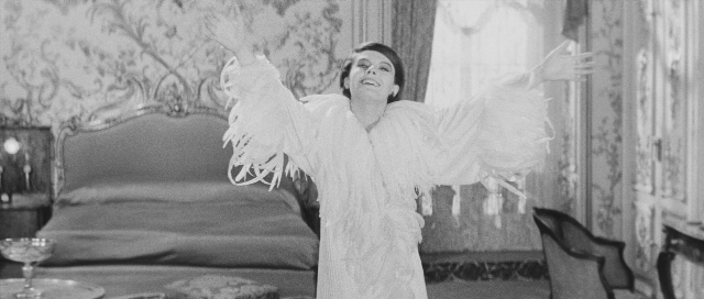 Wide shot frame from L'année dernière à Marienbad — standing, room, bed