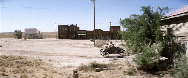 Wide shot frame from There Will Be Blood — street, car, house