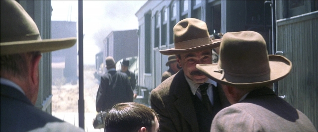 Wide shot frame from There Will Be Blood — standing, hat, suit