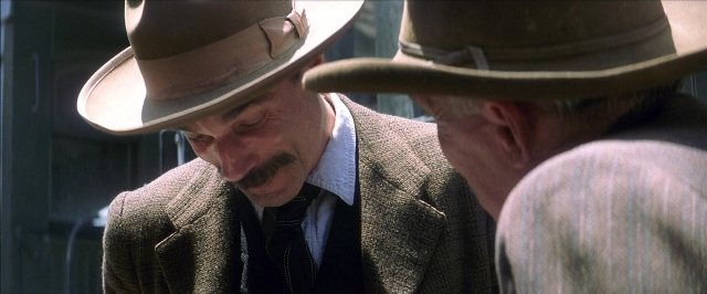 Wide shot frame from There Will Be Blood — standing, hat, suit