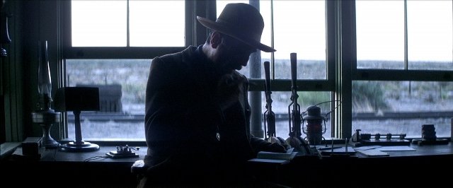 Wide shot frame from There Will Be Blood — sitting, phone, hat