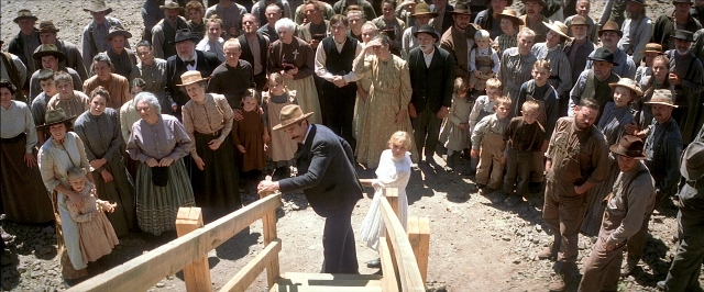 Wide shot frame from There Will Be Blood — standing, hat, suit