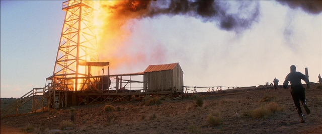 Wide shot frame from There Will Be Blood — fire, hand, suit