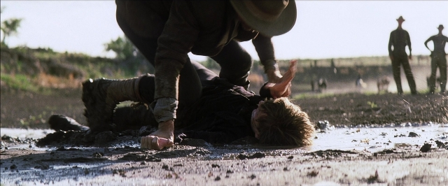 Wide shot frame from There Will Be Blood — standing, hat, hand