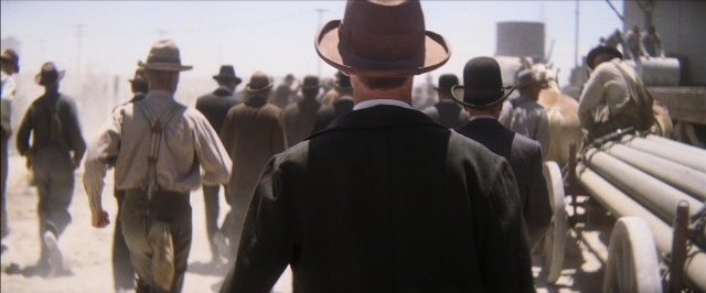 Wide shot frame from There Will Be Blood — walking, street, hat