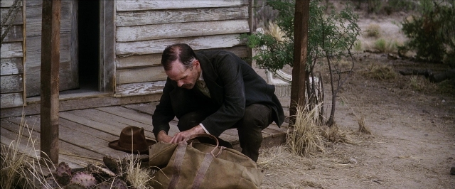 Wide shot frame from There Will Be Blood — door, hat, suit