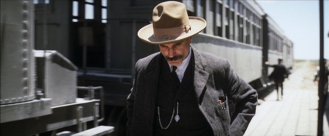 Wide shot frame from There Will Be Blood — standing, hat, coat