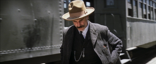 Wide shot frame from There Will Be Blood — standing, hat, car