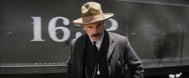 Wide shot frame from There Will Be Blood — standing, hat, suit