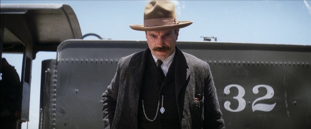 Frame from There Will Be Blood — standing, hat, car