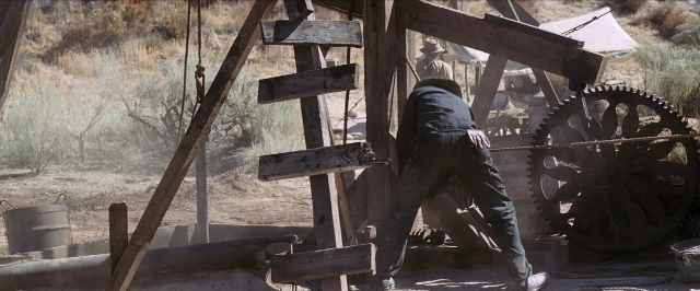 Wide shot frame from There Will Be Blood — standing, hat, wheel