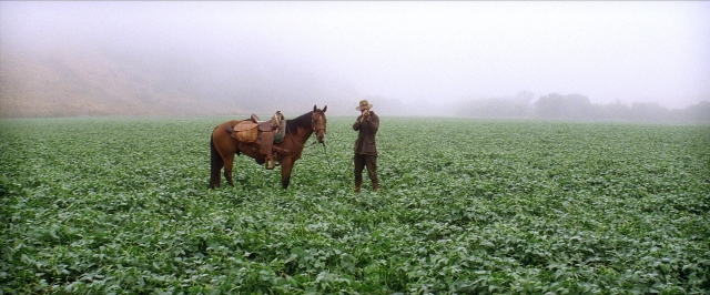 Wide shot frame from There Will Be Blood — standing, hat, coat