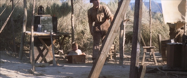 Wide shot frame from There Will Be Blood — sitting, standing, table