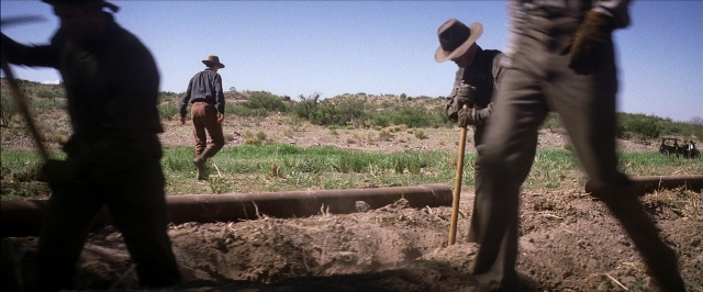 Wide shot frame from There Will Be Blood — standing, walking, pipe
