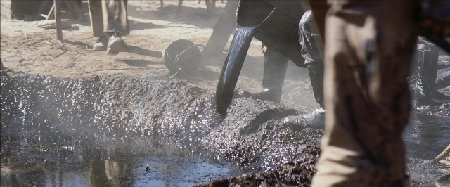 Wide shot frame from There Will Be Blood — hat, hand, water