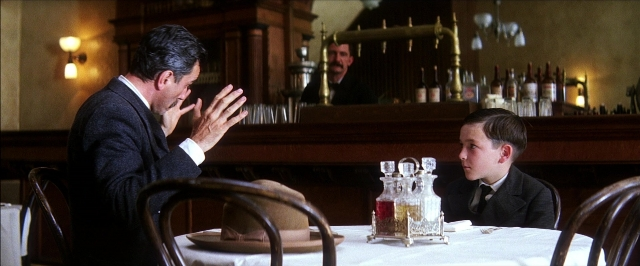 Wide shot frame from There Will Be Blood — sitting, table, suit