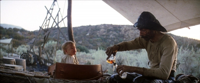 Wide shot frame from There Will Be Blood — sitting, hat, hand