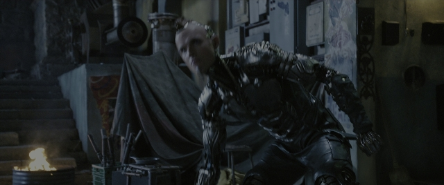 Wide shot frame from Alita: Battle Angel — sitting, room, fire