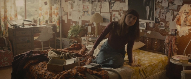 Wide shot frame from The Diary of a Teenage Girl — sitting, book, room
