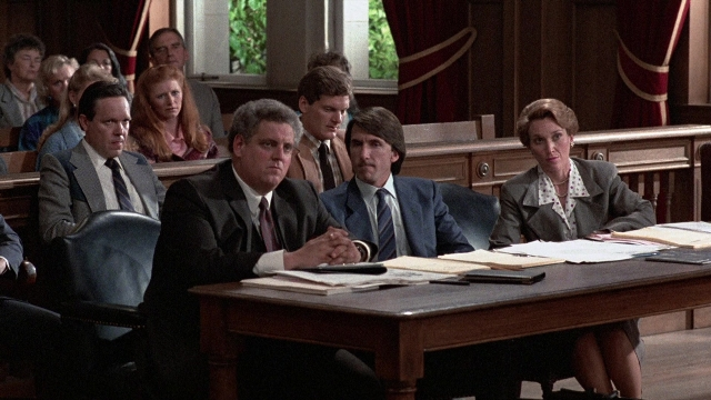 Wide shot frame from The Accused — sitting, table, suit
