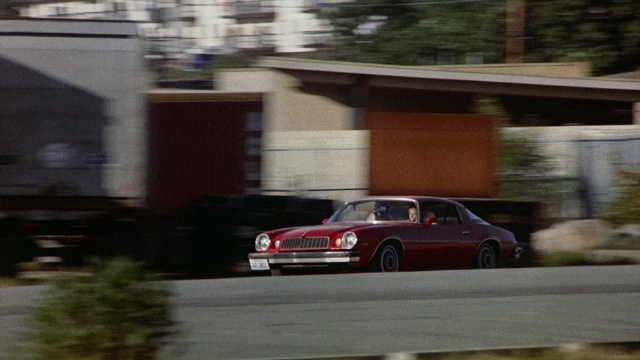 Wide shot frame from The Accused — door, street, car