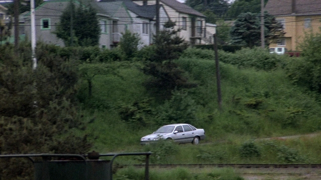 Wide shot frame from The Accused — street, car, house