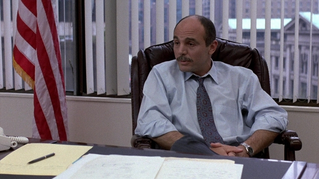 Wide shot frame from The Accused — sitting, phone, flag