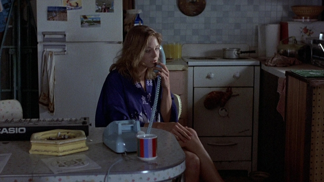 Wide shot frame from The Accused — sitting, phone, kitchen