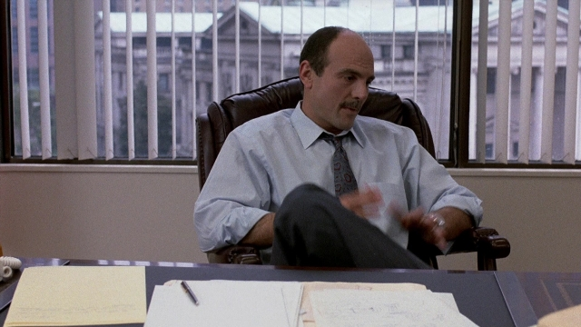 Wide shot frame from The Accused — sitting, table, tie
