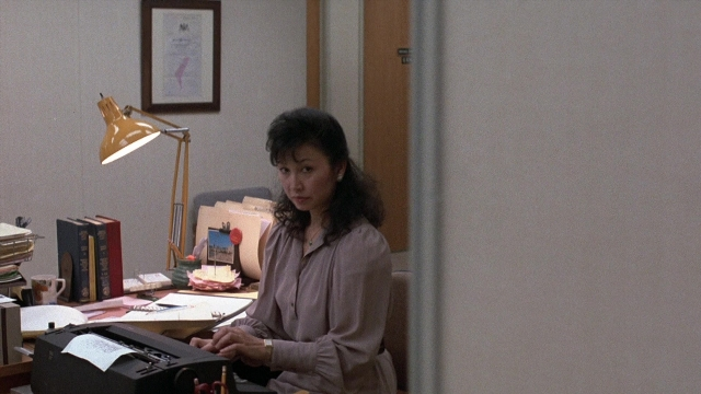 Wide shot frame from The Accused — sitting, desk, room