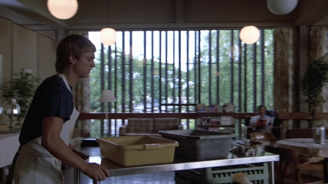 Wide shot frame from The Accused — standing, table, kitchen