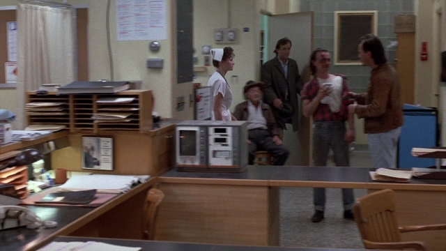 Wide shot frame from The Accused — sitting, desk, book