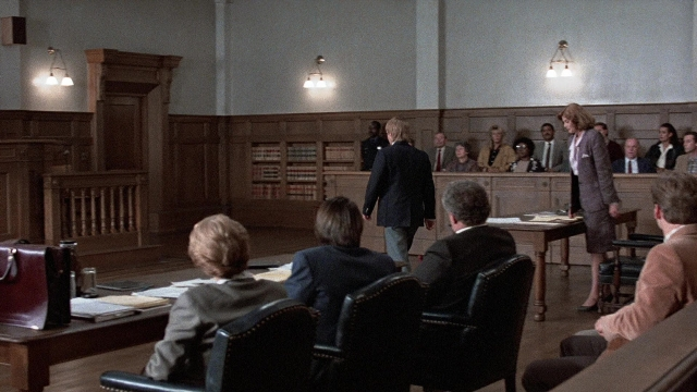 Wide shot frame from The Accused — sitting, standing, room