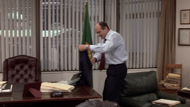 Wide shot frame from The Accused — standing, table, hand