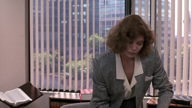 Wide shot frame from The Accused — sitting, book, suit