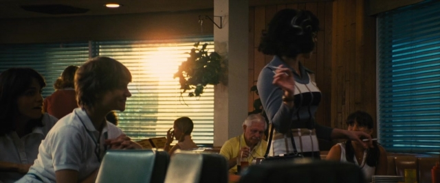 Wide shot frame from Battle of the Sexes — sitting, standing, table
