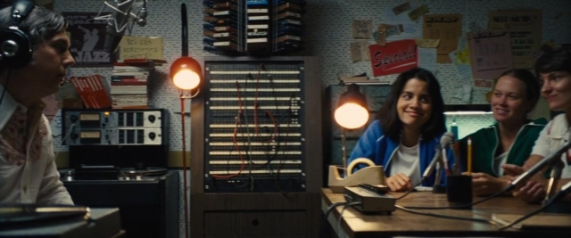 Wide shot frame from Battle of the Sexes — sitting, desk, book