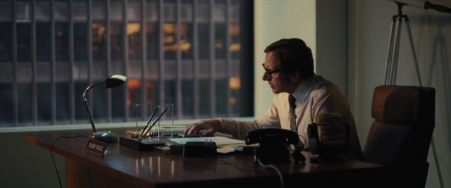Wide shot frame from Battle of the Sexes — sitting, desk, phone