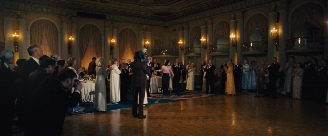 Wide shot frame from Battle of the Sexes — standing, room, table