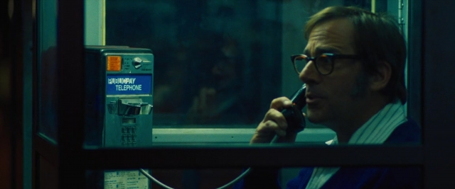 Medium shot frame from Battle of the Sexes — sitting, phone, suit
