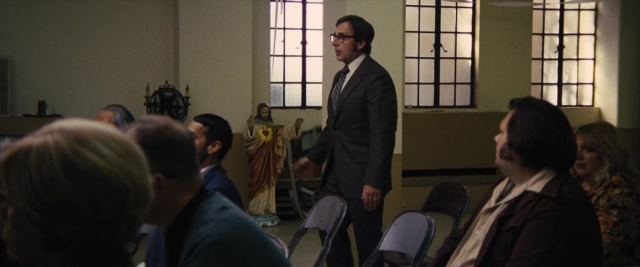 Wide shot frame from Battle of the Sexes — sitting, standing, suit