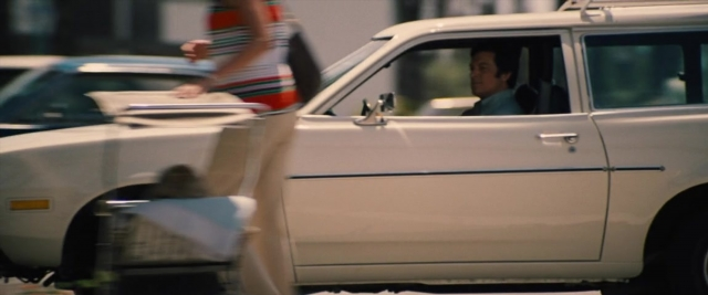 Wide shot frame from Battle of the Sexes — sitting, walking, street