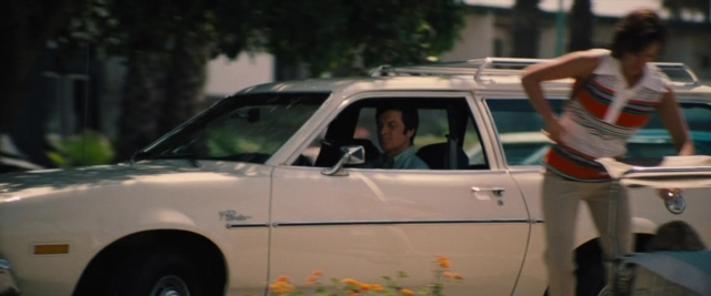 Wide shot frame from Battle of the Sexes — sitting, standing, street