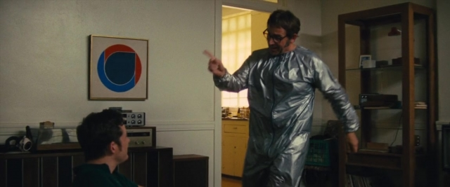 Wide shot frame from Battle of the Sexes — sitting, standing, room