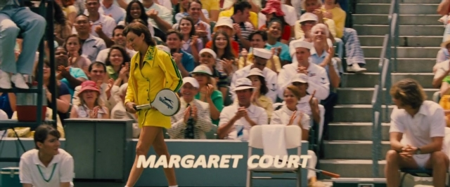 Wide shot frame from Battle of the Sexes — sitting, standing, hand