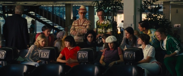 Wide shot frame from Battle of the Sexes — sitting, standing, hat
