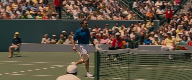 Wide shot frame from Battle of the Sexes — sitting, standing, hand