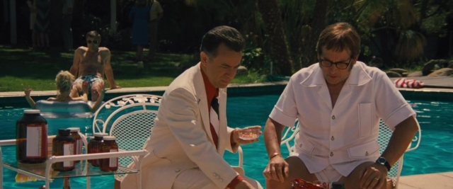 Wide shot frame from Battle of the Sexes — sitting, standing, suit