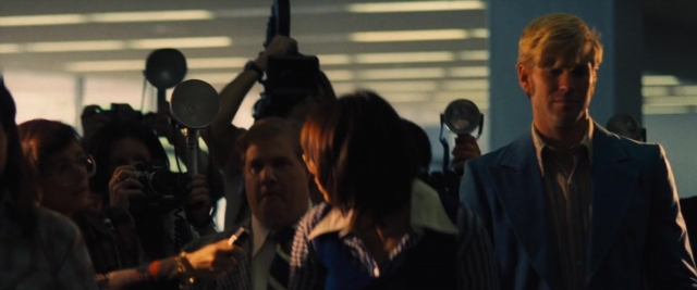 Wide shot frame from Battle of the Sexes — walking, suit, microphone
